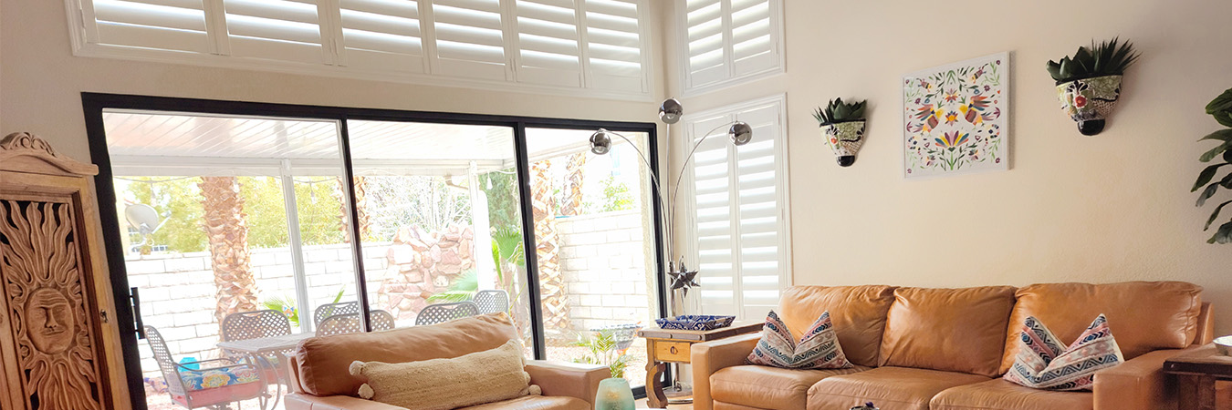 Living room with leather furniture with windows covered by plantation shutters and a nation door going out to the patio.