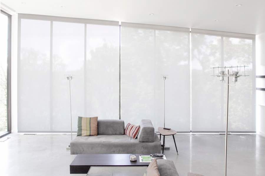 Motorized window shades make controlling natural light effortless in your Denver great room. White motorized shades on a wall of tall great room windows